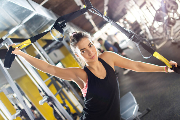 Spor salonunda askılarla egzersiz yapan genç bir kadın.. - Fotoğraf, Görsel