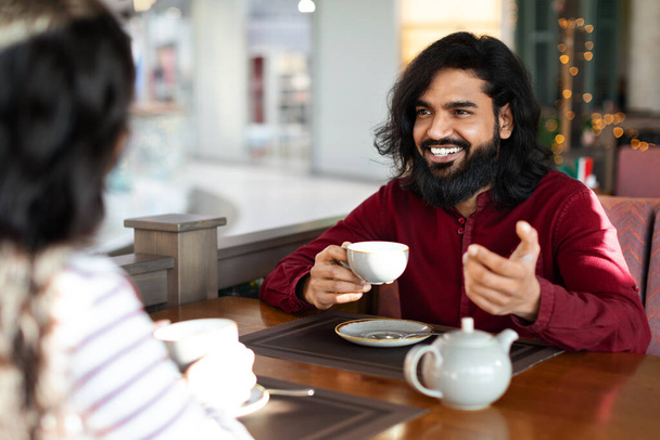 Przystojny Indianin z dziewczyną delektujący się aromatyczną kawą i prowadzący przyjazną rozmowę w miejskiej kawiarni. Romantyczna wschodnia para na pierwszej randce w stołówce, poznawanie się nawzajem - Zdjęcie, obraz