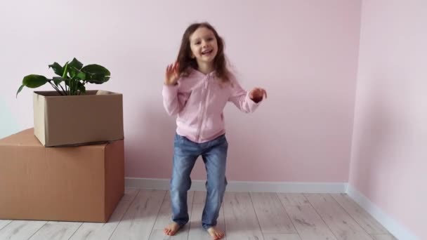Een klein meisje danst graag in de buurt van de dozen met dingen, zich verheugend in haar nieuwe huis. Nieuwe huisvesting. Onroerend goed en verhuur, lening en hypotheek, bedrijfsverplaatsingsdag concept. Langzame beweging. - Video
