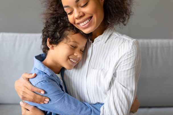 Nahaufnahme einer Mutter und ihres Sohnes, die sich umarmen und beide in einem Innenraum lächeln - Foto, Bild