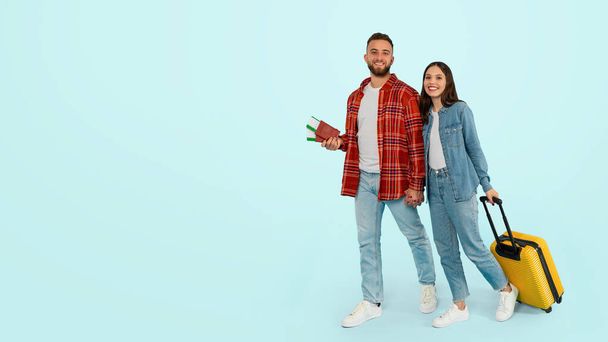 Smiling couple holding tickets and passports walking in studio on blue backdrop, anticipating holiday adventure. Boyfriend and girlfriend posing with travel documents. Panorama, free space - Photo, Image