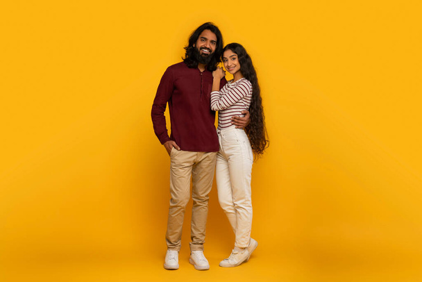 Energetic and excited, the couple points away, drawing attention to something off-camera on the lively yellow backdrop - Photo, Image