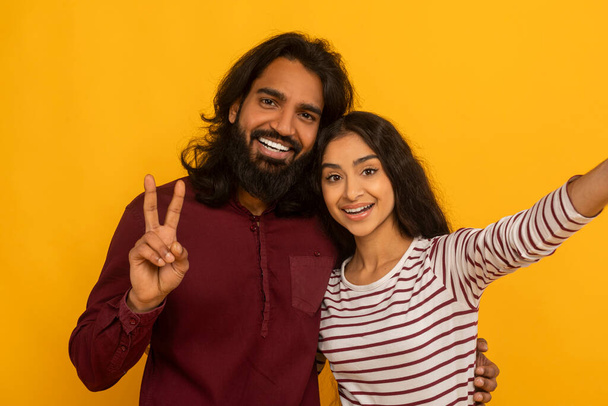 Animated couple taking a selfie with woman flashing a peace sign, both smiling warmly on yellow background - Photo, Image