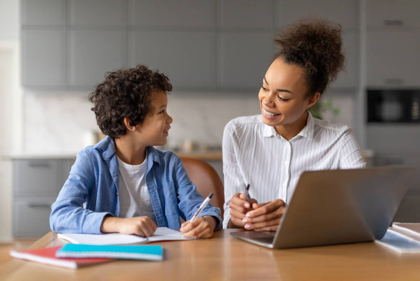 Anya segít a fiának a tanulásban egy laptop előtt egy meleg otthoni környezetben. - Fotó, kép