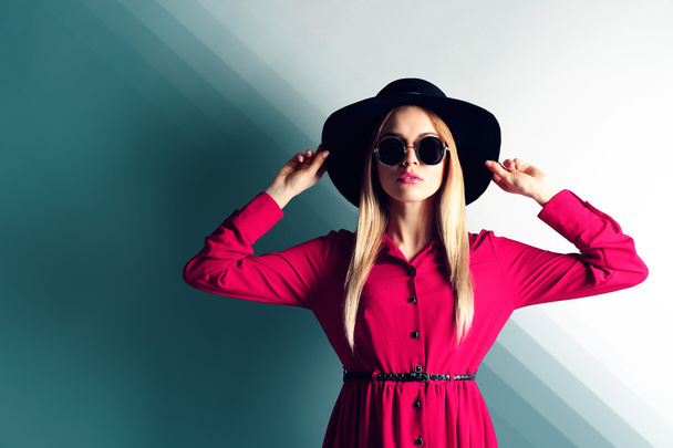 Expressive young model with hat and sunglasses on wall background - Foto, imagen