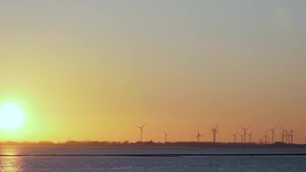 Панорама ветряной электростанции на берегу залива на закате. Ветропарк, Эолийская ферма. Ветряные турбины, генерирующие возобновляемые источники зеленой электроэнергии, защитить окружающую среду, копировать пространство - Кадры, видео