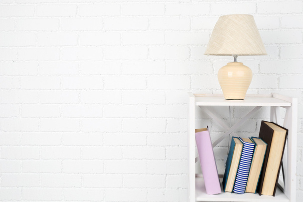 Wooden shelf with books and lamp on brick wall background - Valokuva, kuva