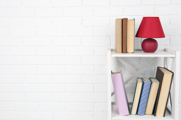 Wooden shelf with books and lamp on brick wall background - Foto, Imagen