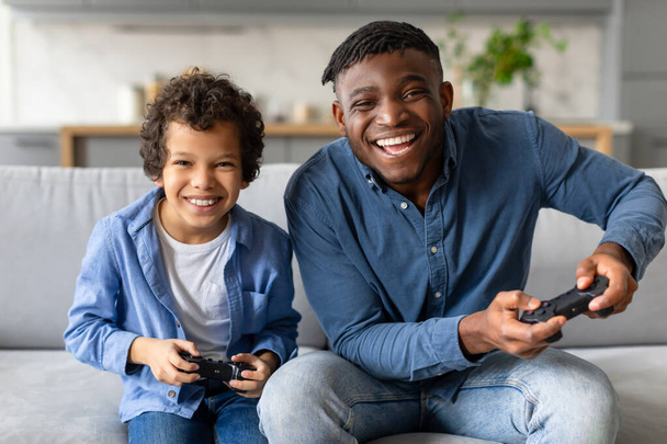 Gioioso padre e figlio si divertono a giocare ai videogiochi insieme in un accogliente soggiorno - Foto, immagini