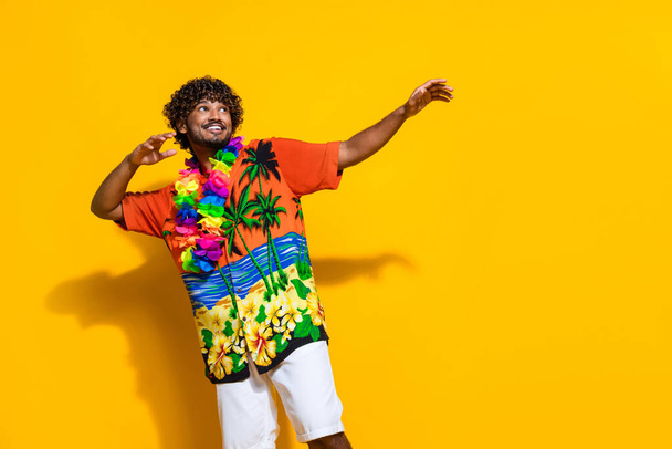 Portrait of nice guy with afro hair wear hawaii flower necklace dancing look at discount empty space isolated on yellow color background. - Фото, зображення