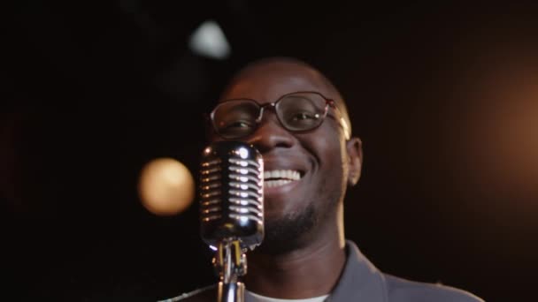 Грудь молодого афроамериканского комика, разговаривающего с аудиторией в микрофон во время выступления с монологом на темной сцене - Кадры, видео