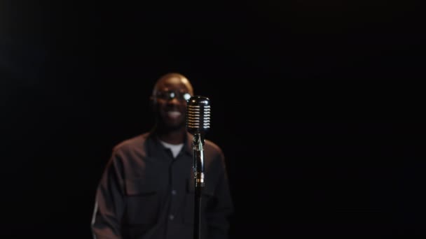 Medium slowmo shot van jonge zwarte mannelijke standup komiek naderen retro microfoon op donker podium, begroeten publiek en beginnen met het uitvoeren van - Video