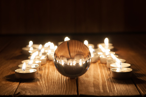 Boule transparente en verre et bougies allumées sur un vieux fond en bois
 - Photo, image