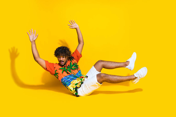 Full length photo of funny astonished guy wear hawaii shirt white sneakers hands up falling down isolated on yellow color background. - Fotografie, Obrázek