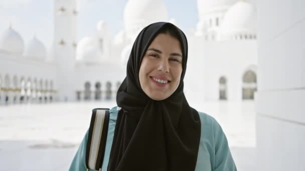Una donna sorridente in hijab posa davanti alla grandiosa moschea dello sceicco Zayed in Abu Darren sotto il cielo limpido. - Filmati, video