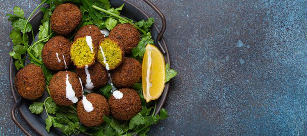 Plate of fried falafel balls served with fresh green cilantro and lemon top view on rustic concrete background. Traditional vegan dish of Middle Eastern cuisine, space for text - Photo, Image