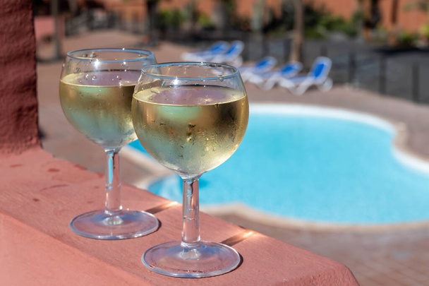 Szemüveg hideg fehér bor a tetőteraszon szolgált szabadtéri, kilátás Corralejo, Fuerteventura a napsütéses napon, medence kék vízzel - Fotó, kép