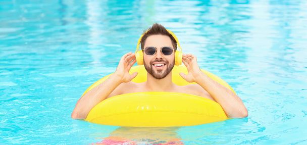 Genç adam yüzme havuzunda müzik dinliyor. - Fotoğraf, Görsel
