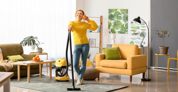 Young woman listening to music while hoovering floor at home - Photo, Image