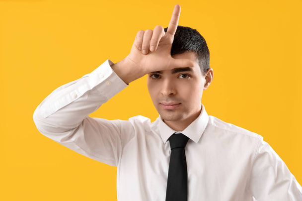 Giovane uomo d'affari che mostra gesto perdente su sfondo giallo, primo piano - Foto, immagini