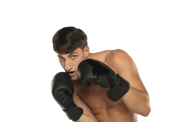 Νεαρός γυμνόστηθος άνδρας με γάντια πυγμαχίας σε λευκό φόντο στούντιο - Φωτογραφία, εικόνα