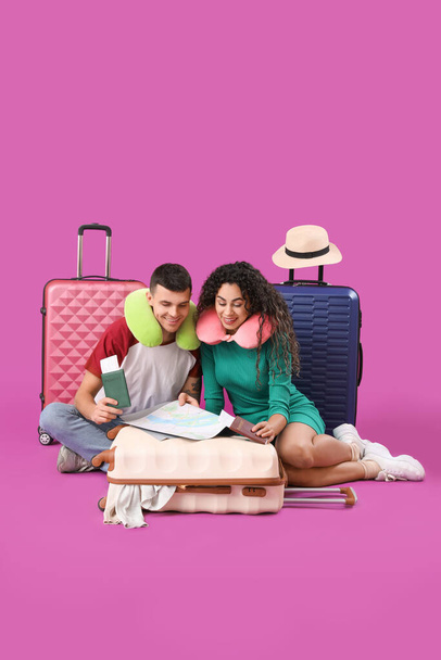 Couple de touristes avec valises et carte assis sur fond rose - Photo, image
