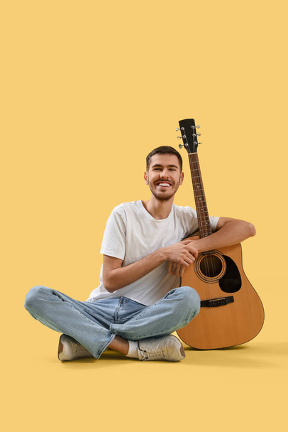 Handsome young man with guitar on yellow background - Photo, Image