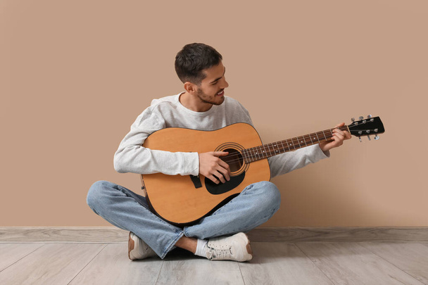 Knappe jongeman speelt gitaar op beige achtergrond - Foto, afbeelding