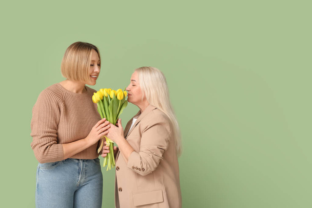 Eine erwachsene Frau begrüßt ihre Mutter mit einem Strauß Tulpen auf grünem Hintergrund. Feier zum Internationalen Frauentag - Foto, Bild