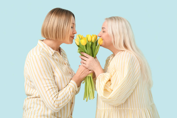 Mujer adulta saludando a su madre con ramo de tulipanes sobre fondo azul. Celebración del Día Internacional de la Mujer - Foto, imagen
