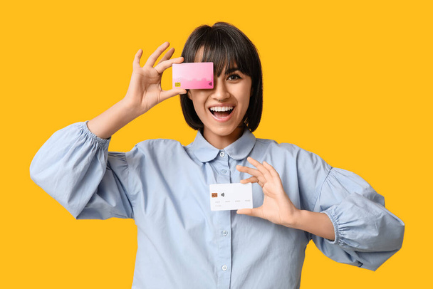 Glückliche junge Frau mit Kreditkarten auf gelbem Hintergrund - Foto, Bild