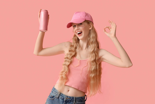 Mooie jonge vrouw met blikje frisdrank tonen ok gebaar op roze achtergrond - Foto, afbeelding