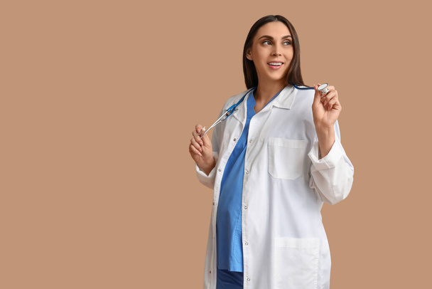 Красивый молодой беременный врач со стетоскопом на коричневом фоне - Фото, изображение