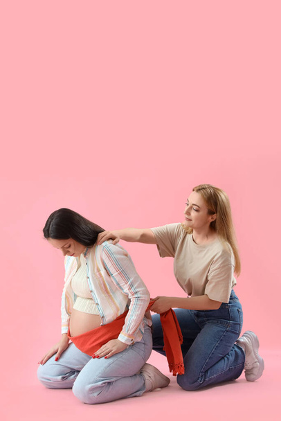 Зріла дула масажує вагітної жінки з шарфом на рожевому фоні - Фото, зображення