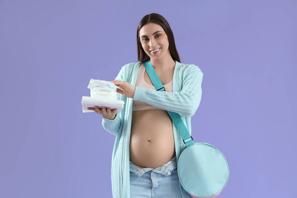 Mladá těhotná žena s plenkami a porodnice nemocniční taška na šeříku pozadí - Fotografie, Obrázek