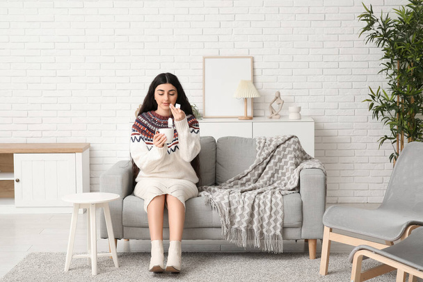 Όμορφη νεαρή γυναίκα με φλιτζάνι ζεστό τσάι στον καναπέ στο σπίτι - Φωτογραφία, εικόνα