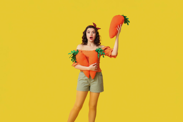 Emotionele pin-up vrouw met speelgoed wortels op gele achtergrond - Foto, afbeelding