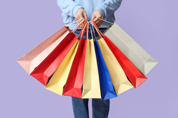 Mujer joven con muchas bolsas de compras sobre fondo lila - Foto, imagen