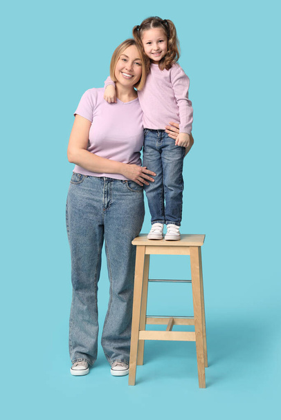 Szczęśliwa matka i jej dziecko stojące na krześle na niebieskim tle. Dzień Matki - Zdjęcie, obraz