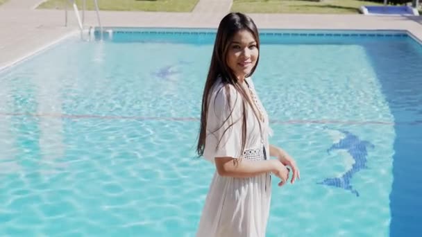 Una donna elegante in un abito bianco alla moda si erge a bordo piscina sotto il sole spagnolo, evocando un senso di lusso, svago e vibrazioni estive.. - Filmati, video