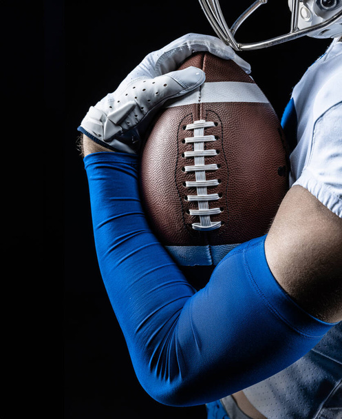 Close-up studiofoto van een Amerikaanse voetballer die stevig aan een voetbal vasthoudt. Goede generieke American Football foto - Foto, afbeelding