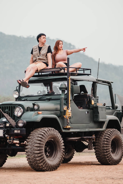 Couple aventureux est perché au sommet d'une voiture robuste, la femme pointant vers l'horizon, prêt pour leur prochaine exploration hors route. - Photo, image