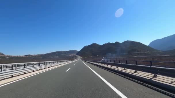 Un coche está viajando en un camino de asfalto con formas terrestres montañosas en el fondo, creando un paisaje pintoresco con el cielo que se encuentra con el horizonte - Metraje, vídeo