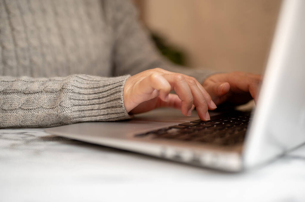 Uno scatto ritagliato di una donna in un maglione accogliente che lavora sul suo computer portatile, digitando sulla tastiera del computer portatile e navigando in Internet. persone e concetti tecnologici - Foto, immagini