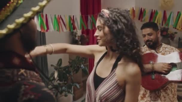 Medium close-up slowmo schot van jonge Mexicaanse mensen die plezier hebben op huisfeest - man in sombrero houden meisjes hand, gelukkig meisje swirling rond, en man in helder shirt spelen gitaar - Video
