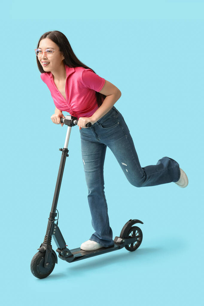 Šťastný mladý asijské žena na koni moderní elektrický kick scooter na modrém pozadí - Fotografie, Obrázek