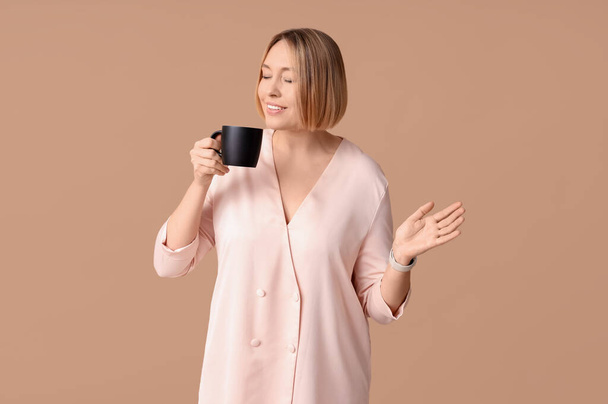 Ευτυχισμένη ενήλικη γυναίκα με φλιτζάνι καφέ σε μπεζ φόντο - Φωτογραφία, εικόνα