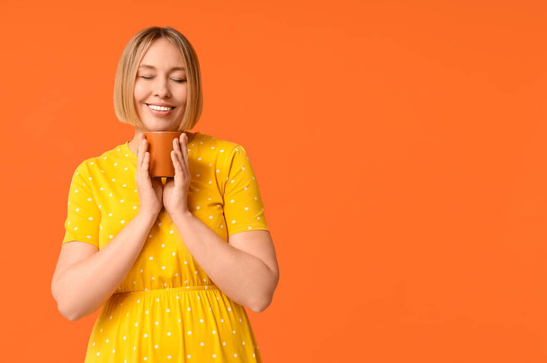 Счастливая взрослая женщина с чашкой кофе на оранжевом фоне - Фото, изображение