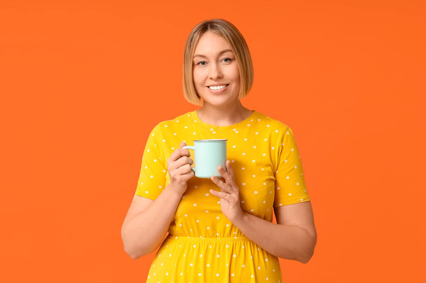 Happy adult woman with cup of coffee on orange background - Photo, Image