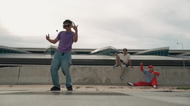 Група азіатських танцюристів-перерв виконують вуличні танці з підтримкою мультикультурного друга та рухомою хіп-хоп музикою. Привабливий красивий хіпстер практикує танець хлопчика на вулиці. Спорт на відкритому повітрі 2024 року. Спрінгсі. - Кадри, відео